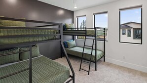 Une chambre avec un lit superposé, un ventilateur de plafond, de grandes fenêtres et une vue sur les maisons environnantes.