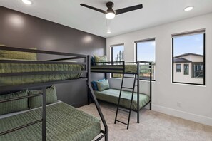 A bunk bed room with a ceiling fan, large windows, and a view of houses outside. - Luxury Moab Oasis Pool, Spa & Fire Pit (Moab)