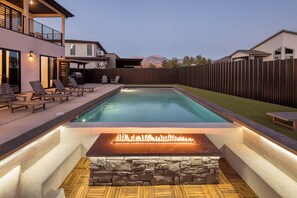 A rectangular swimming pool with a stone surround and a built-in fire feature.