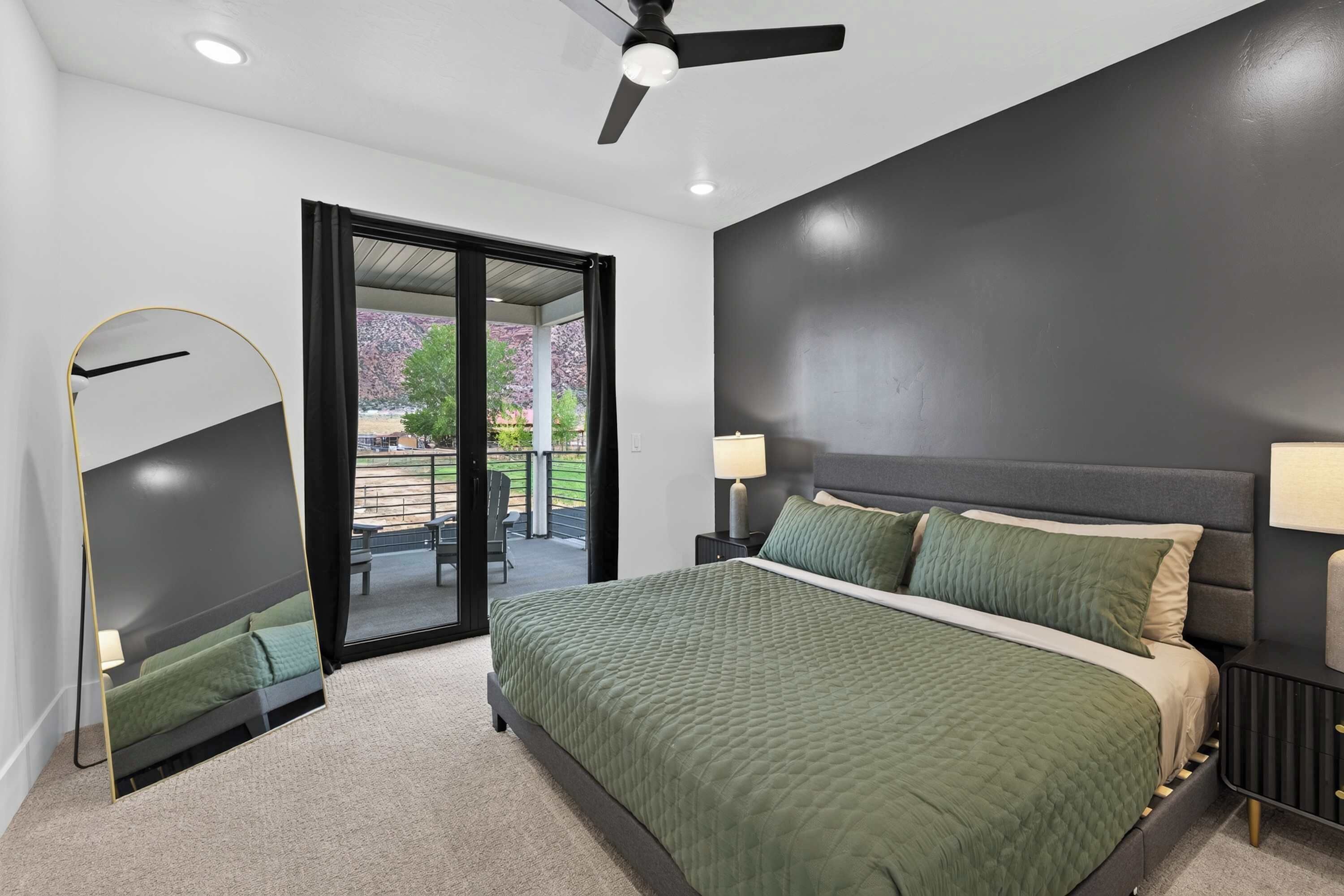 A bedroom with a bed, a ceiling fan, a nightstand, a lamp, and a view of the outdoors through a sliding door.