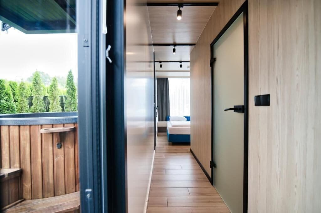 Ein Korridor mit Holzboden, der zu einem Zimmer mit Bett und Fenster führt.