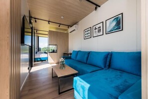 Un interior moderno con un sofá azul, una mesa de madera y una cocina visible a través de una puerta abierta.