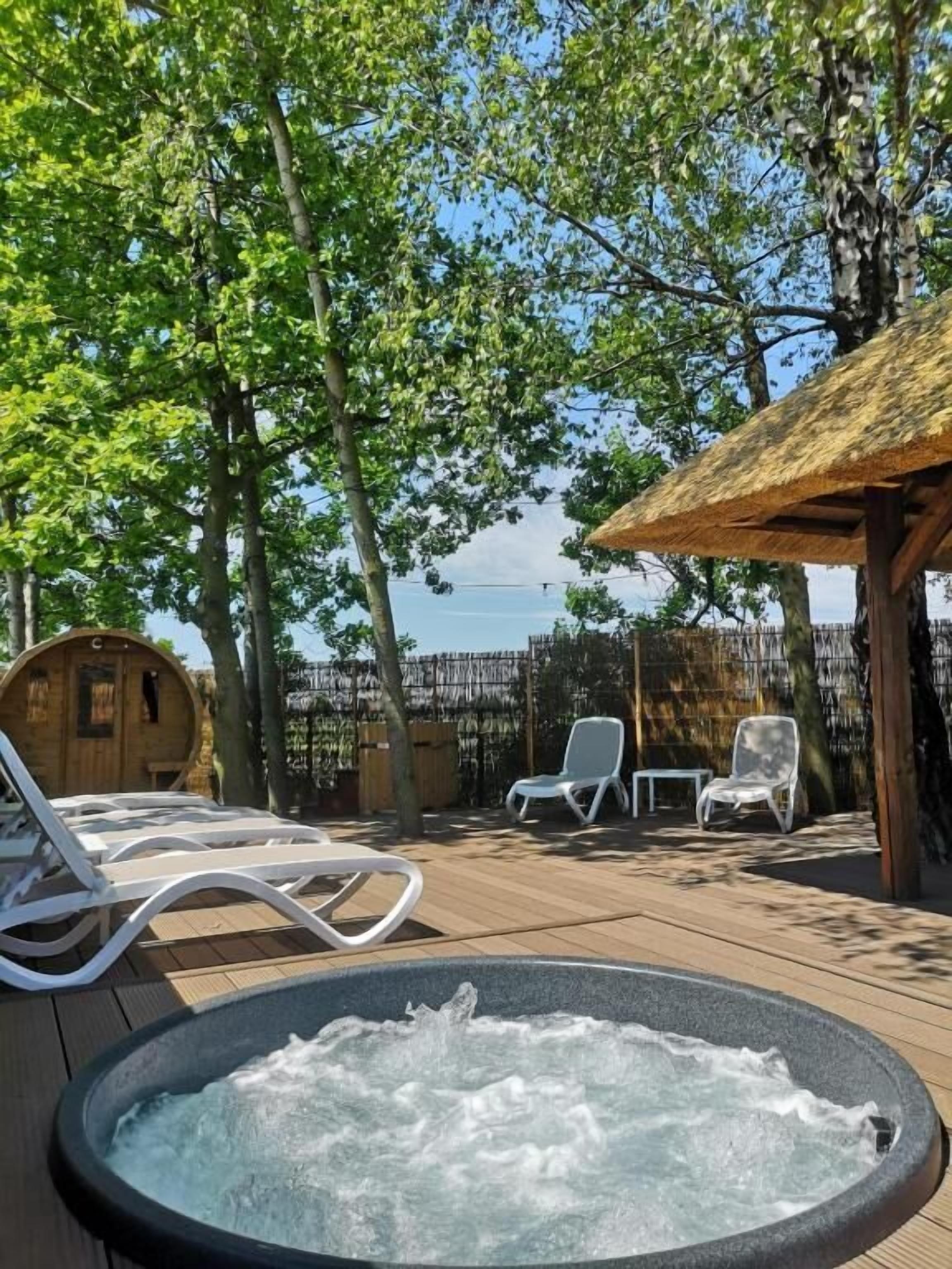 Ein Whirlpool umgeben von Liegestühlen und einer Holzterrasse, mit Blick auf das Meer im Hintergrund.