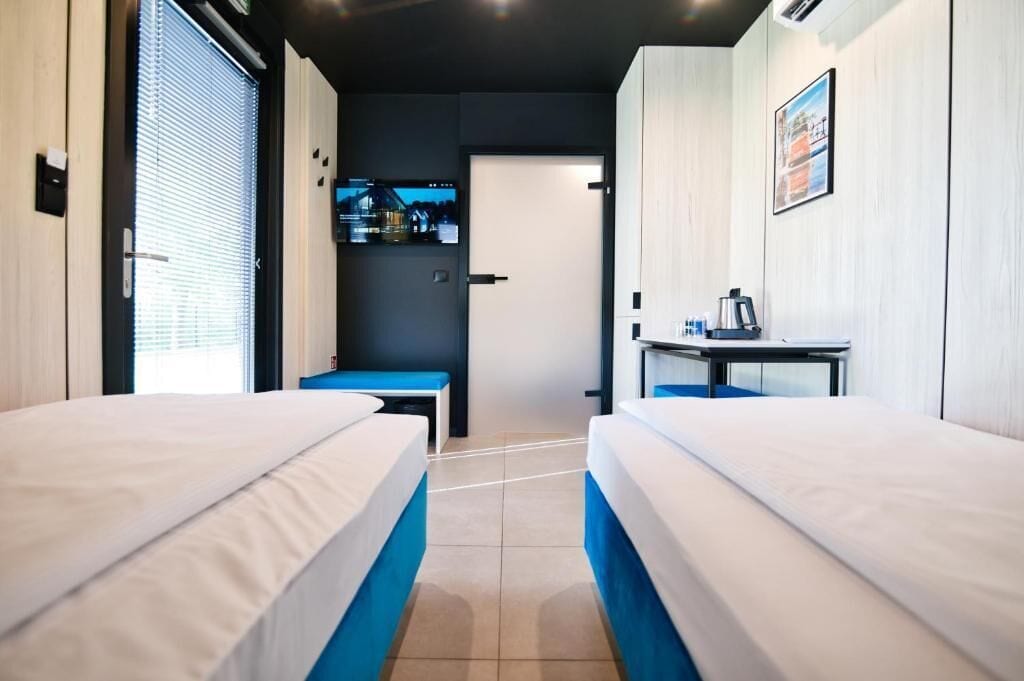 Habitación de hotel con dos camas, un escritorio con silla, televisión y una puerta que da a otra habitación.