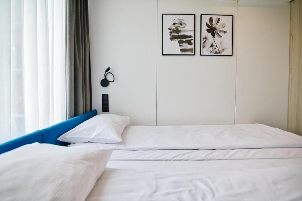 Una habitación de hotel con dos camas, una ventana con cortinas y dos cuadros enmarcados en la pared.