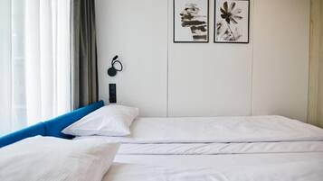 Una habitación de hotel con dos camas, una ventana con cortinas y dos cuadros enmarcados en la pared.