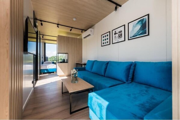 A modern interior with a blue sofa, a wooden table, and a bed with a view.