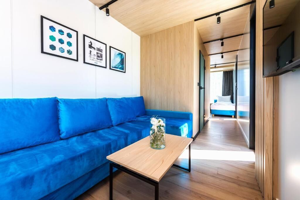 A modern interior with a blue sofa, a wooden table with a vase, and framed artwork on the wall.