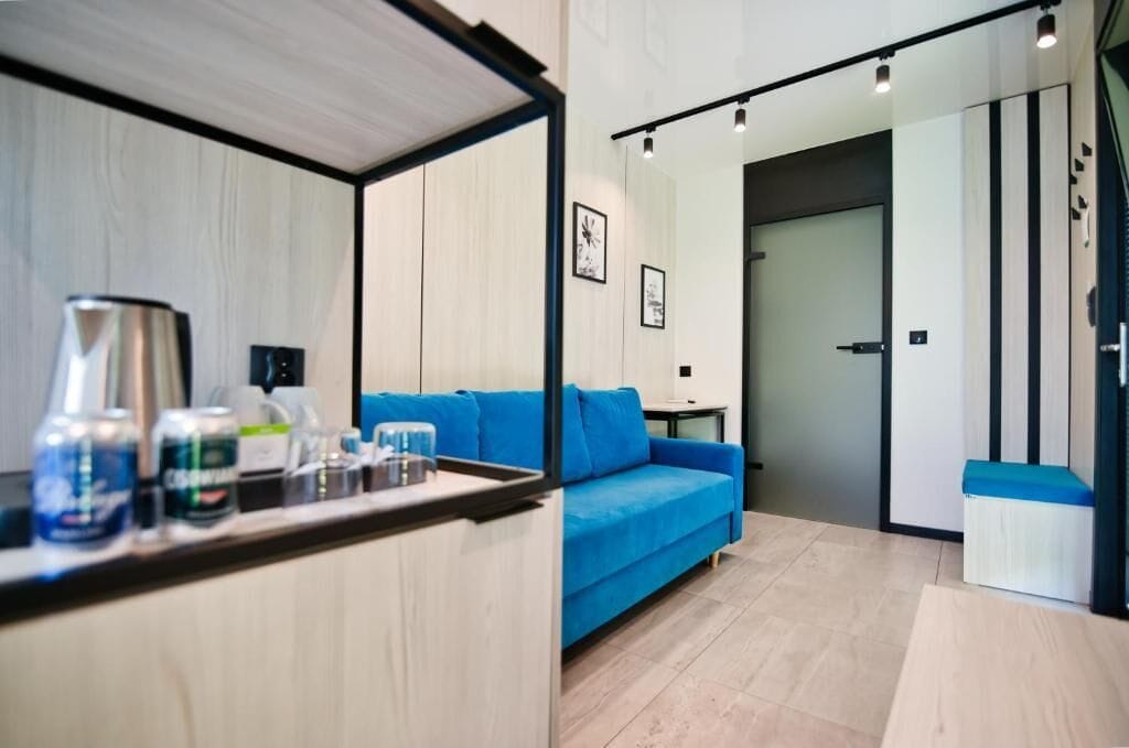 Ein modernes Hotelzimmer mit einem blauen Sofa, einer Kaffeemaschine und einem kleinen Tisch mit diversen Gegenständen.