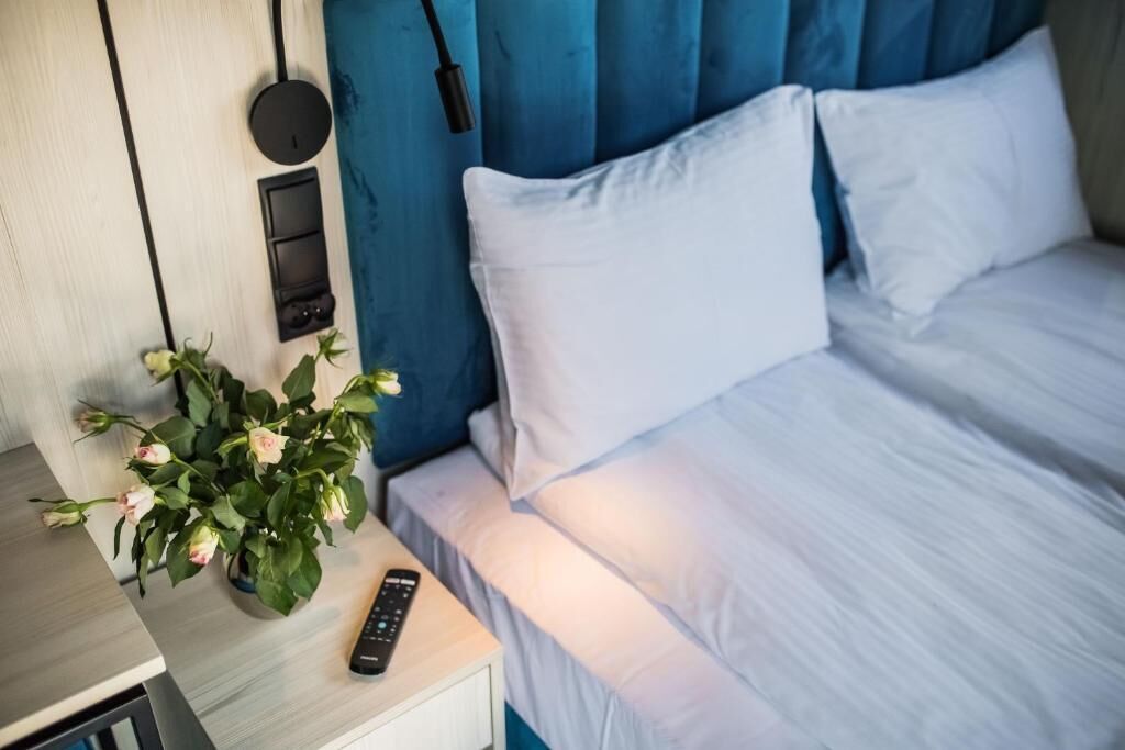 Ein Bett mit weißer Bettwäsche, ein Nachttisch mit Fernbedienung und ein Topf mit Blumen.