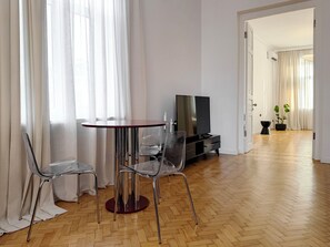 Una sala de estar moderna con una mesa redonda, dos sillas, un televisor de pantalla plana y una planta en maceta.