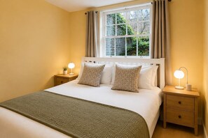 Een slaapkamer met een bed, twee nachtkastjes, een raam met gordijnen en een nachtkastje met een lamp.