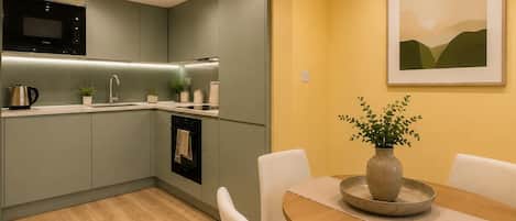 Una cocina moderna con microondas, estufa y pileta, un comedor con mesa y sillas, y un cuadro en la pared.