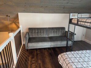 Une pièce avec un canapé gris, un lit superposé et une rambarde blanche.