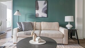 A living room with a beige sofa, a round coffee table, and a framed abstract artwork on the wall. - Landing | Stunning 2BD, Gym, Clubhouse (Houston)