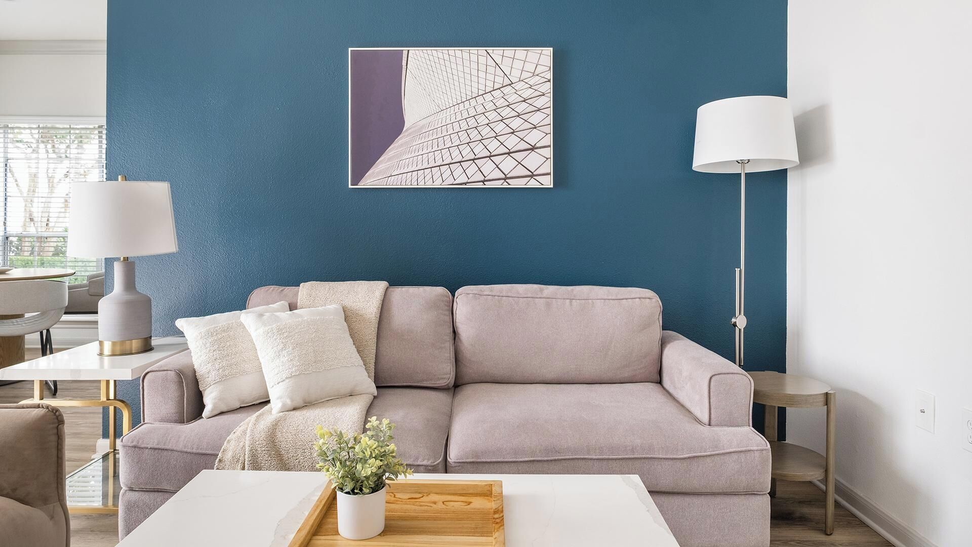 A modern living room with a blue accent wall, a grey sofa, a white coffee table, and a floor lamp.