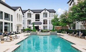 A swimming pool with lounge chairs, a fountain, and a multi-story building with balconies. - Landing | Stylish 1BD, Clubhouse, Pool (Houston)