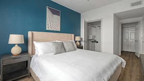 Quarto com uma cama, mesas de cabeceira, uma obra de arte na parede e uma porta que dá para o banheiro.
