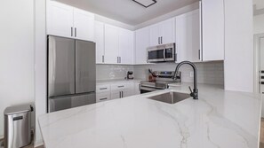 A modern kitchen with white cabinets, stainless steel appliances, and a marble countertop. - Landing | Stylish 2BD, Yoga Studio, Clubhouse (Houston)