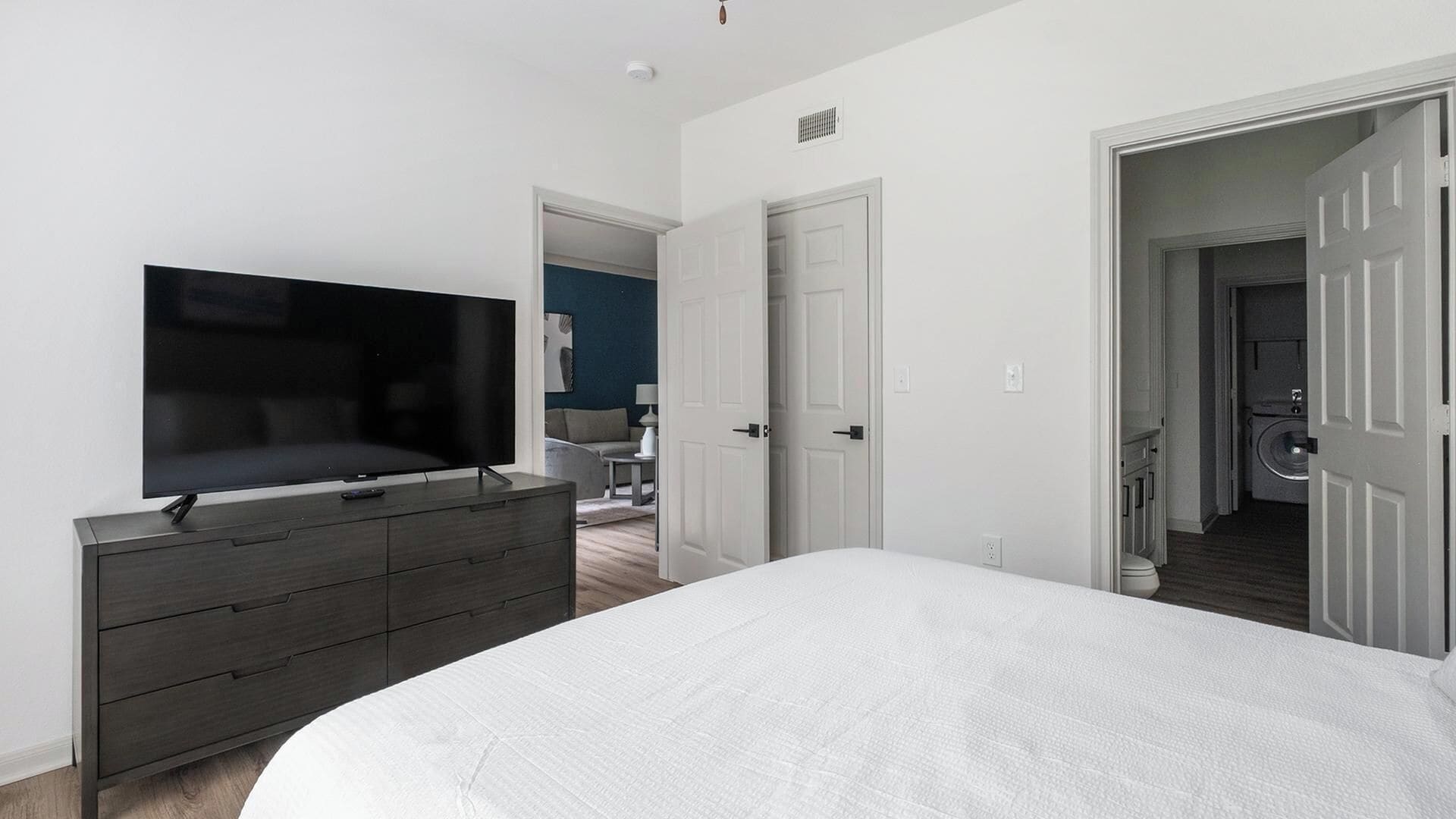 Um quarto com cama, penteadeira, televisão e porta para um banheiro.