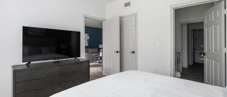 A bedroom with a bed, dresser, TV, and a door leading to a bathroom.
