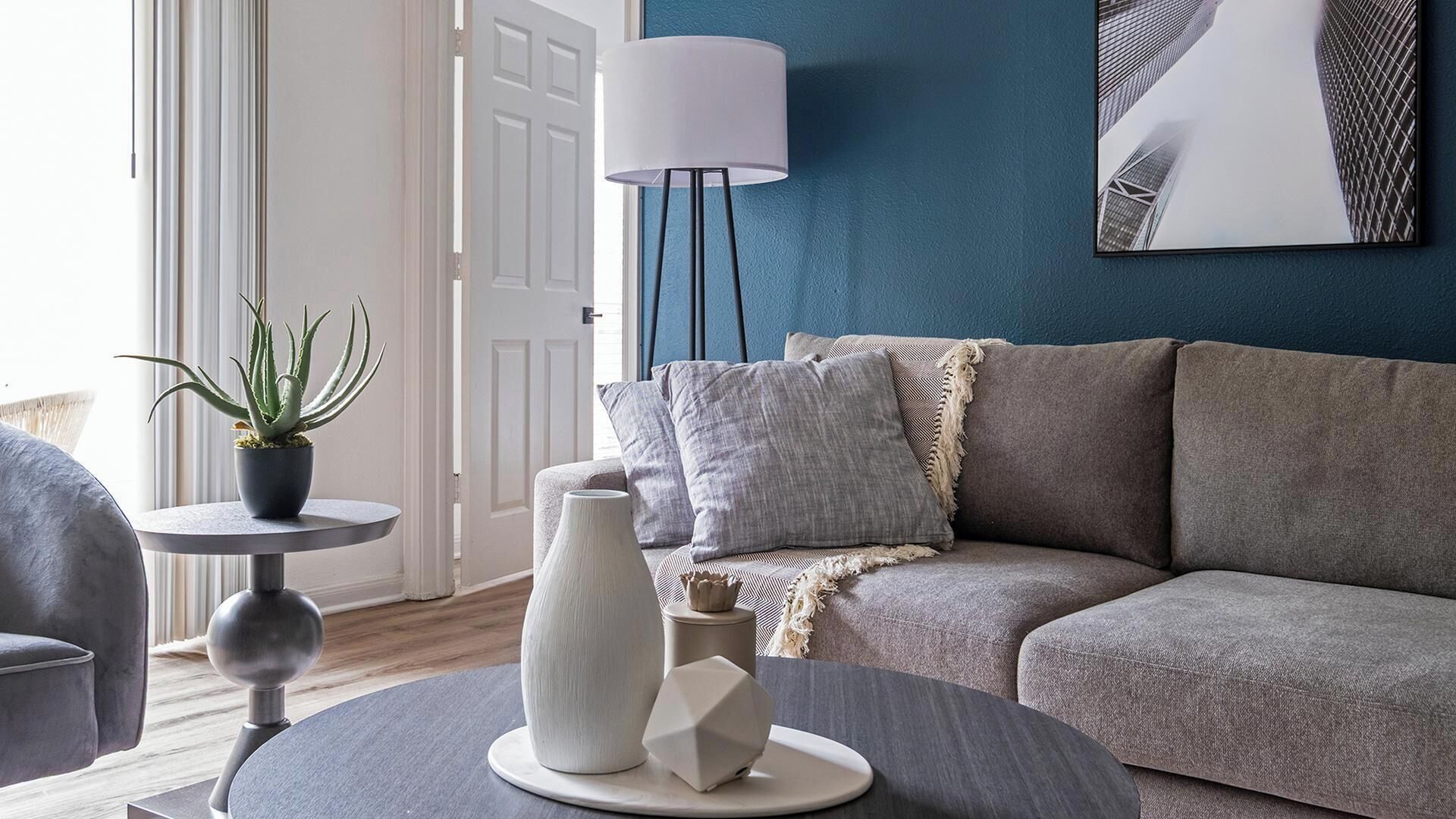 A living room with a grey sofa, a round coffee table, a potted plant, and a floor lamp.