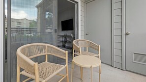 Ein Zimmer mit zwei Korbstühlen, einem kleinen runden Tisch, einem Fernseher an der Wand und einer Glastür zum Balkon.