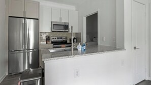 A modern kitchen with stainless steel appliances, a granite countertop, and white cabinetry. - Landing | Modern 1BD, Clubhouse, Gym (Austin)