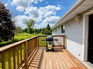 A deck with a grill, a lamp, and a view of a green field.