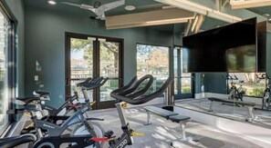 A gym with stationary bikes, a bench, and a large TV screen. - Landing | Modern 2BD, Clubhouse, Gym (Austin)