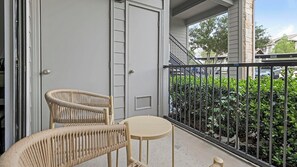 A balcony with two wicker chairs and a small round table, overlooking a hedge and a street. - Landing | Beautiful 1BD, Clubhouse, Gym (Austin)
