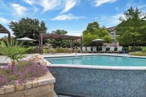 A swimming pool with lounge chairs and umbrellas, surrounded by greenery and a pergola. - Landing | Amazing 1BD, Clubhouse, Gym (Austin)