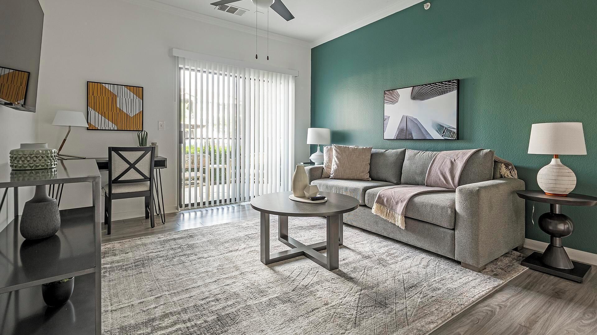 Una sala de estar moderna con un sofá gris, dos mesitas de noche con lámparas, una mesa de centro y un comedor con una silla y mesa.