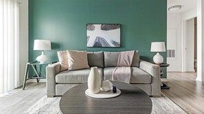 A living room with a teal wall, a gray sofa, two side tables with lamps, and a coffee table with decorative items. - Landing | Amazing 1BD, Clubhouse, Gym (Austin)