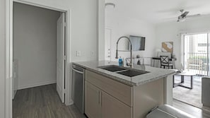A modern kitchen with a built-in sink, a dishwasher, and a dining area with a table and chairs. - Landing | Beautiful 1BD, Clubhouse, Gym (Austin)