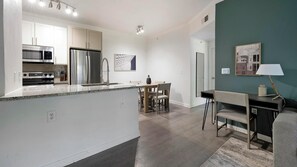 Eine moderne Küche mit Edelstahlgeräten, ein Essbereich mit Tisch und Stühlen sowie ein Wohnbereich mit Sofa und Lampe.