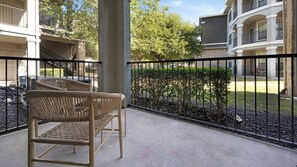 Ein Balkon mit zwei Korbstühlen, einem Metallgeländer und Blick auf benachbarte Gebäude und Grünflächen.