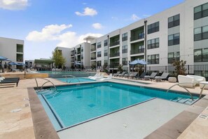 A swimming pool with lounge chairs and a multi-story building in the background. - Landing | Beautiful 2BD, Pool, Gym (Austin)
