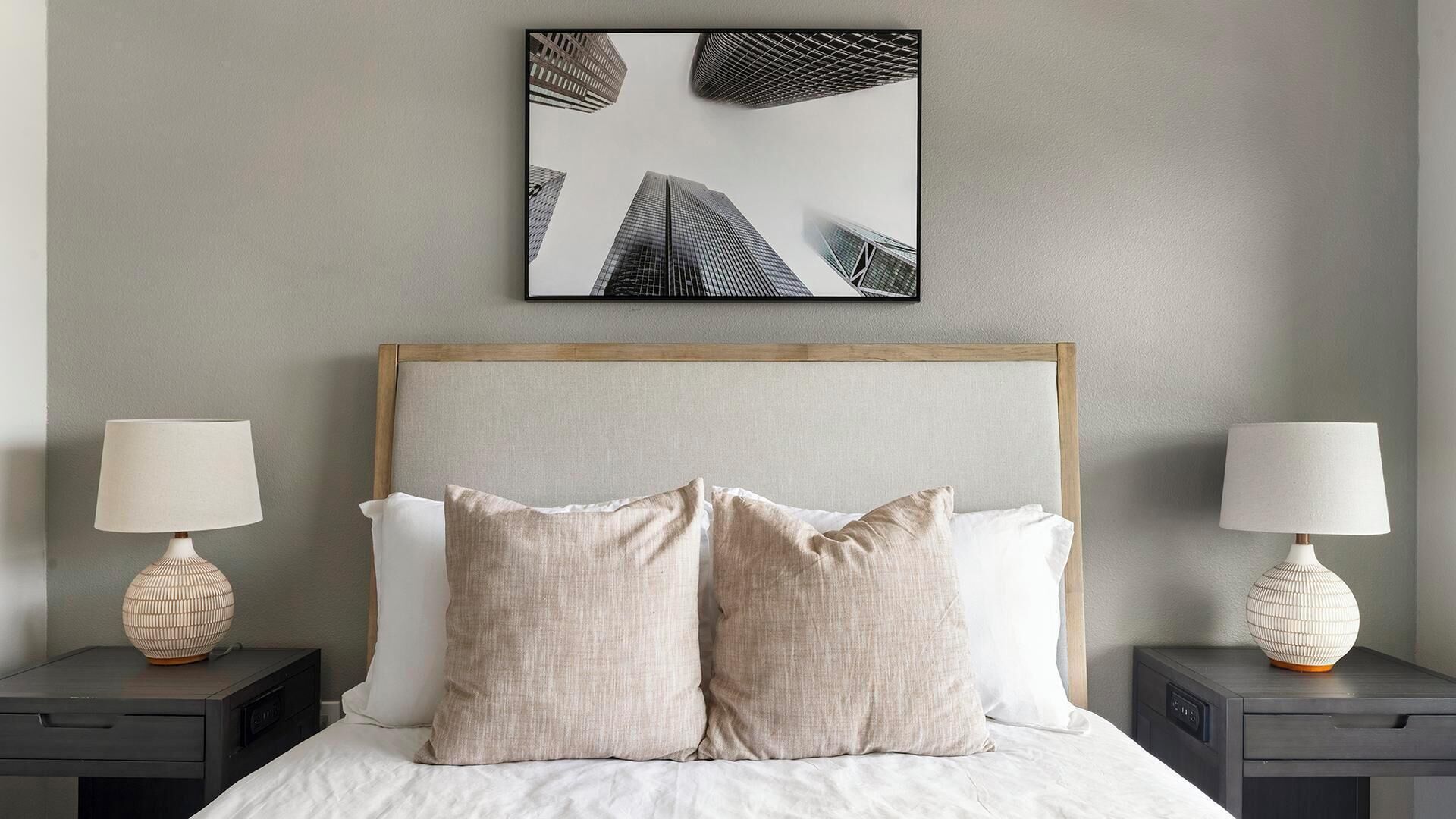 Un dormitorio con una cama, dos mesitas de noche, dos lámparas y un cuadro en la pared.