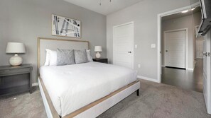 A bedroom with a large bed, two bedside tables, a nightstand, a door, and a hallway. - Landing | Beautiful 2BD, Pool, Gym (Austin)