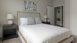 Een slaapkamer met een bed, nachtkastjes, een lamp, een schilderij en een deur.