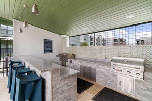 A modern outdoor kitchen with a bar area, a grill, and a seating arrangement. - Landing | Amazing 2BD, Pool, Gym (Austin)
