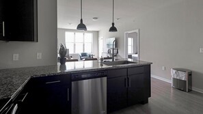 A modern kitchen with a central island, stainless steel appliances, pendant lighting, and a view into the living area. - Landing | Amazing 2BD, Pool, Gym (Austin)
