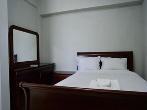 Une chambre d’hôtel standard avec un lit en bois, une table de chevet et un miroir.