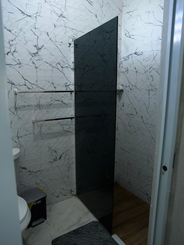 Une salle de bain avec douche, toilettes et une poubelle.
