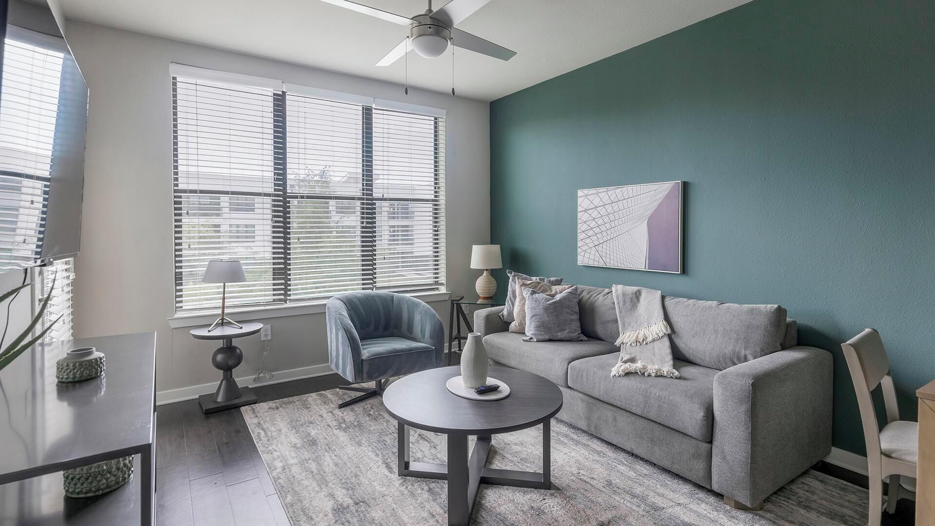 A modern living room with a grey sofa, a round coffee table, and a ceiling fan.
