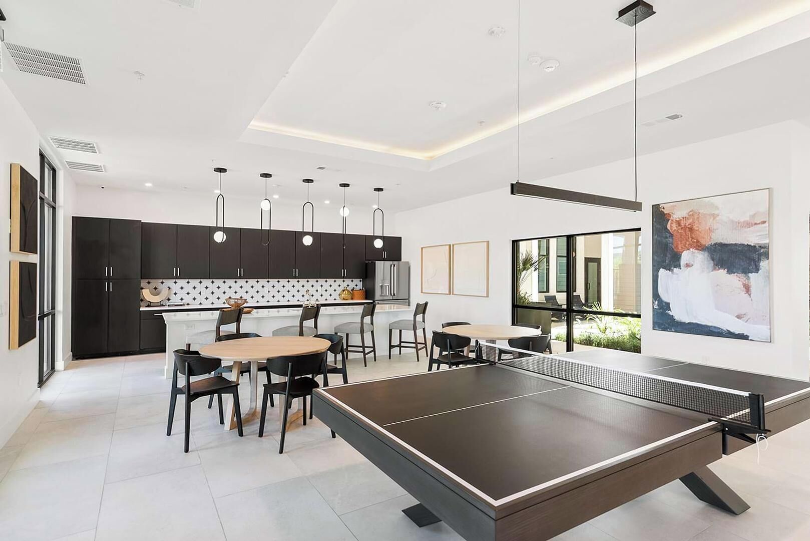 A modern kitchen with dark cabinets, pendant lights, and a dining area with a ping pong table.