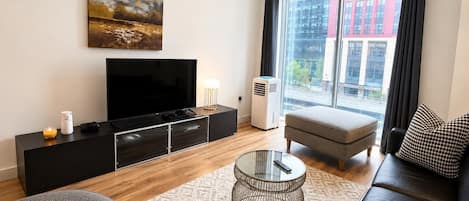 Una sala de estar moderna con un televisor de pantalla plana, un sofá, una mesa de centro y un ventanal con vista a un edificio.