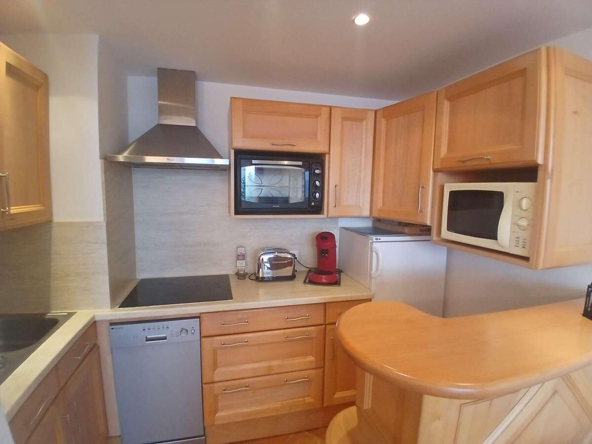 Cocina compacta con armarios de madera, microondas, tostadora y lavavajillas.
