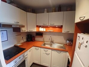 A compact kitchen with white cabinets, a black induction cooktop, a stainless steel sink, and a white refrigerator. - 20m from ski slopes, 1st floor, terrace, tv, ski locker, 70m², Alpe d'Huez (L'Alpe d'Huez)